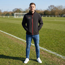 Load image into Gallery viewer, Softshell Jacket in black and red from Scorpion Sports. Photo showing a model wearing the jacket whilst watching sport.
