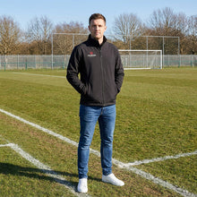 Load image into Gallery viewer, Black Softshell Jacket on a model standing on the side of a pitch watching the game.
