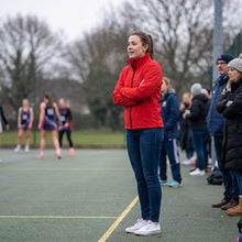 Load image into Gallery viewer, Red Softshell Jacket on a lady watching a netball game. 
